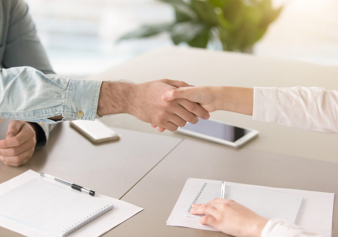 Close up side view of male and female hands shaking above the table. Greeting or congratulating gesture at the meeting, students holding debates, young partners starting a startup